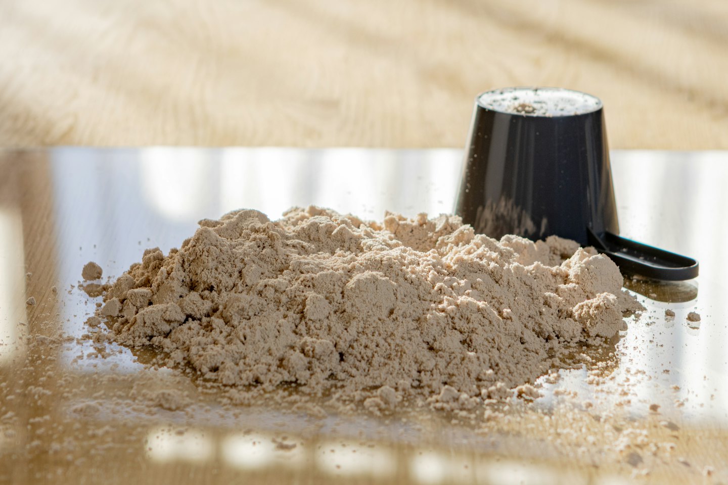 Ein schwarzer Löffel liegt neben einem Haufen hellbraunen Proteinpulvers.