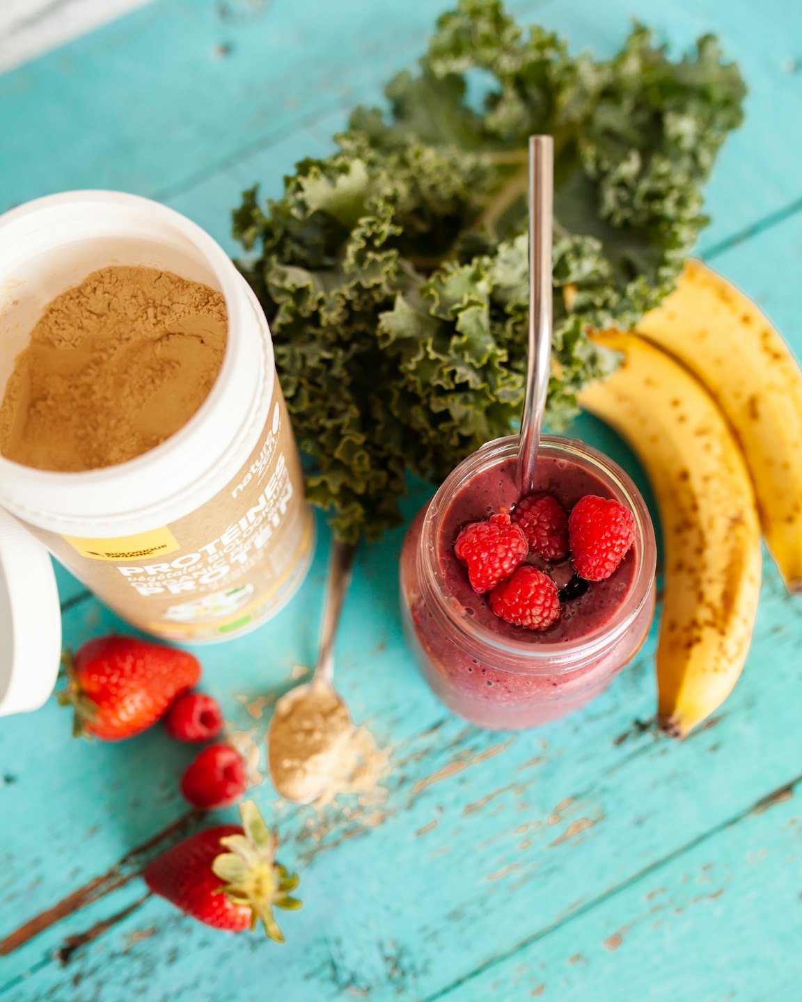 Proteinshake, Bananen, Grünkohl und ein Beeren-Smoothie auf Holz.