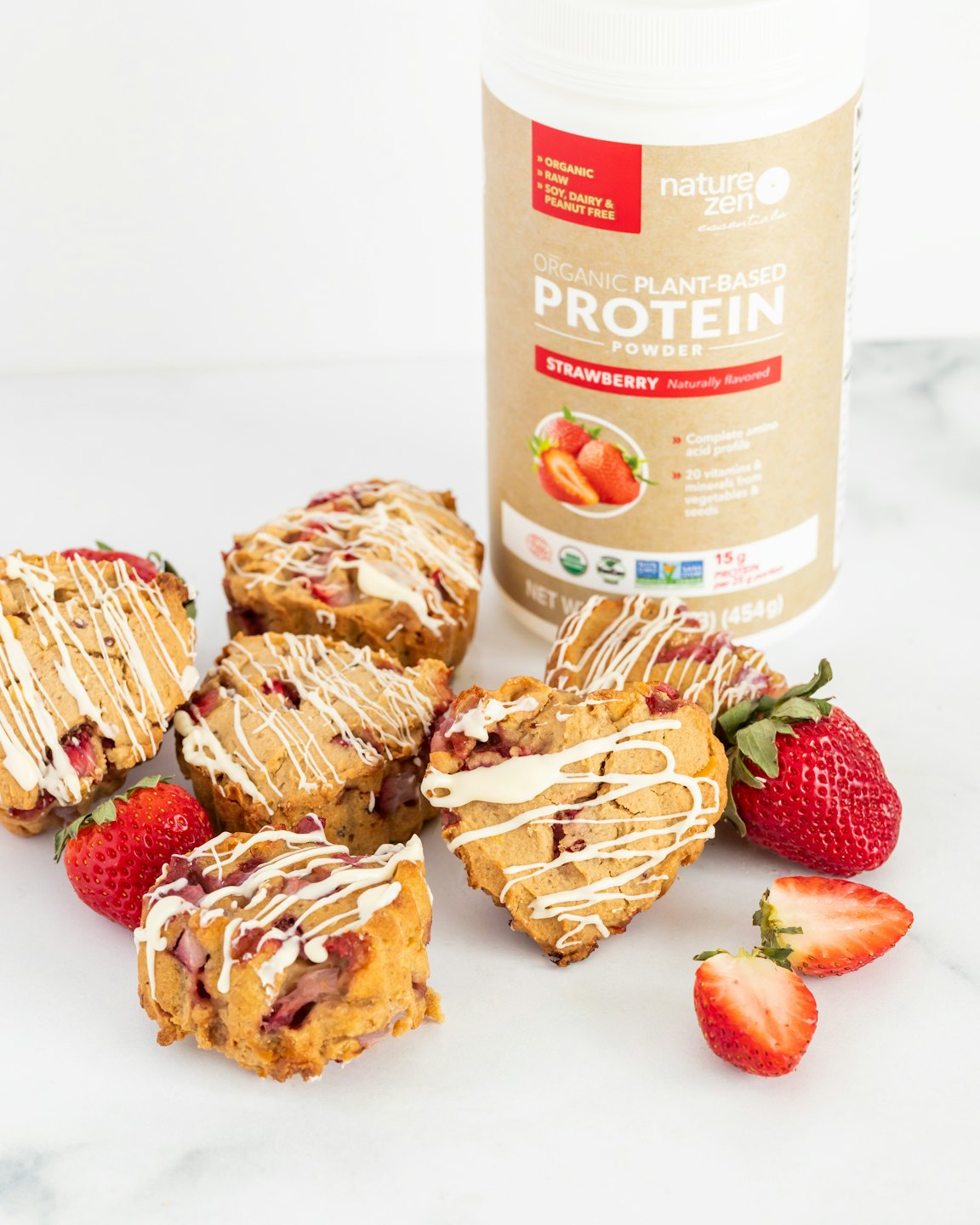 Erdbeer-Proteinpulver-Dose, umgeben von herzförmigen Muffins und frischen Erdbeeren.