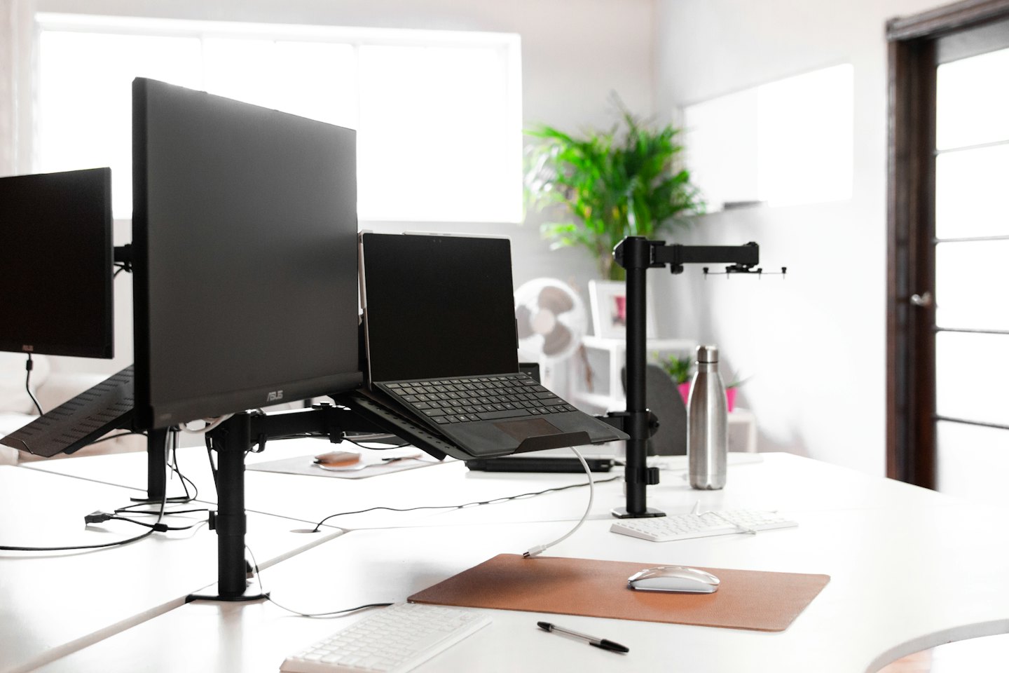 Moderner Büroarbeitsplatz mit mehreren Monitoren und ergonomischen Halterungen.